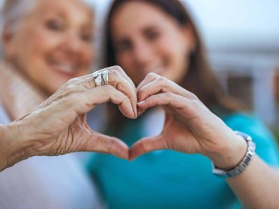 Elderly Woman and Caregiver Forming Heart Shape with Hands