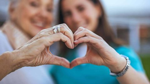 Elderly Woman and Caregiver Forming Heart Shape with Hands