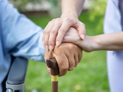 Nurse holding elderly man hand with cane on wheelchair in garden close up