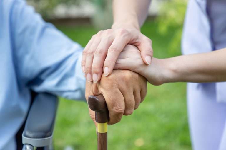 Nurse holding elderly man hand with cane on wheelchair in garden